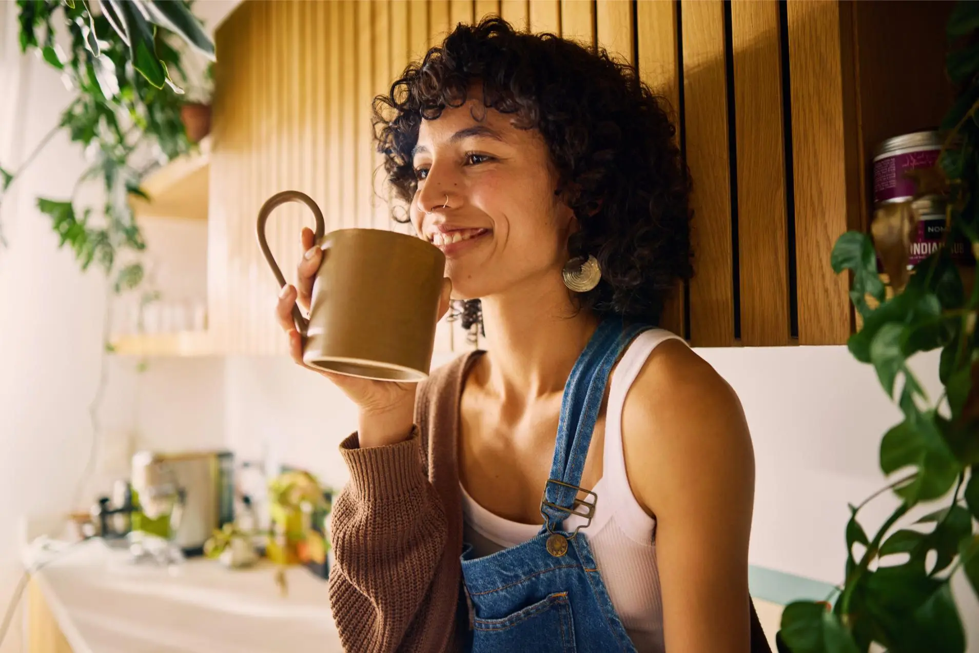 Content Woman Savoring The Aroma Of Her Morning Coffee In A Well-Lit Kitchen With Modern Wooden Accents And Lush Houseplants, Embracing A Moment Of Serenity, Symbolizing Mindfulness And The Joy Of Simple Pleasures In Everyday Life
