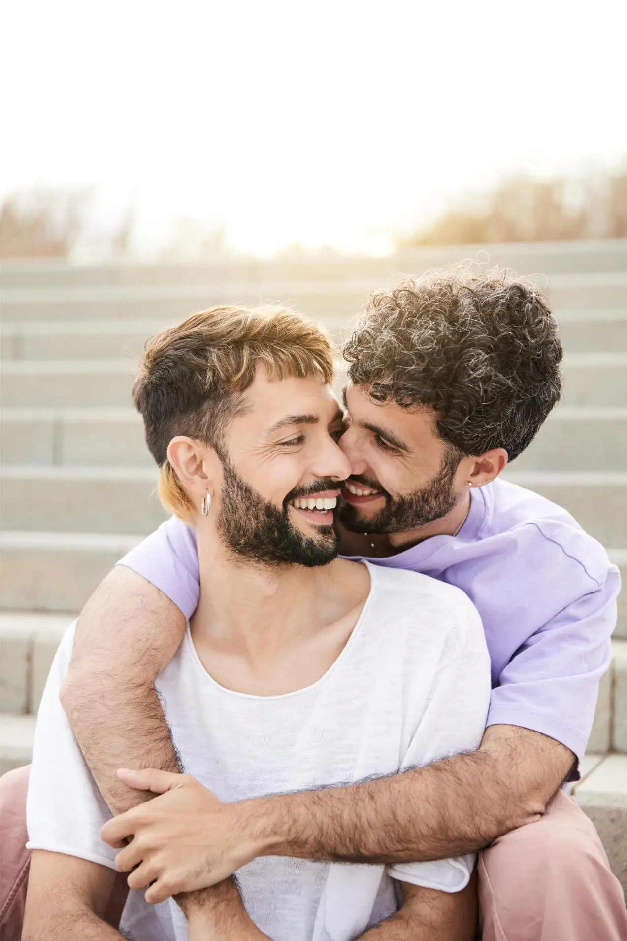 Happy gay couple hugging, joking and having fun in an intimate outdoor embrace. Vertical photo.